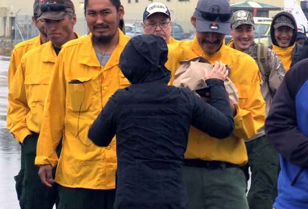 BLM AFS's Kay Kudo, in black, hands two sack lunches to Ernest Barger Jr of Buckland while Tuck Cleveland of Noorvik and Ronald Skin of Selawik wait their turn in line before boarding a plane to the Lower 48 to help with a busy fire season. Each of the 83 boarding the plane on Sunday were given two sack lunches before they left. Photo by Beth Ipsen, BLM AFS.