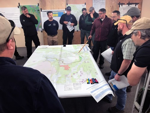 Photo of Casey Boespflug, with pointer, briefs a group of representatives from the BLM Eastern Interior Field Office, State of Alaska, Department of Defense, the Alaska Wildland Fire Coordinating Group, on a strategic plan the Alaska Incident Management Team has been working on for the past few days. Photo by Beth Ipsen, BLM AFS