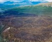 Minimal smoke rises from the Chetaslina Fire (#606) with green vegetation surrounding and the mountain range in the background.