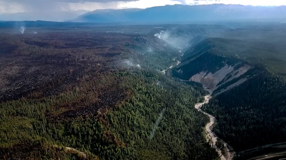 Aerial view of the Chetaslina Fire (#606) showing burned area, green vegetation, minimal smoke, and rain in the distance.