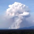 A large smoke plume rises in the horizon.