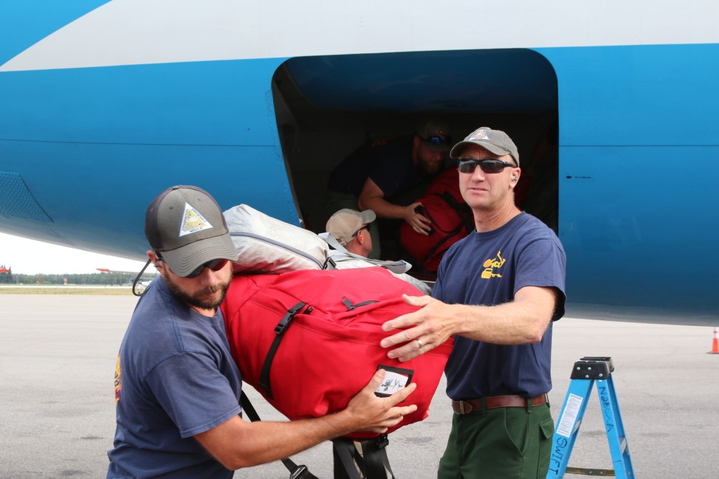 This picture depicts firefighters moving bags of their personal gear out of the cargo hold of an aircraft.