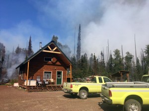 Two Alaska Division of Forestry engines sit in front of a home with smoke from the Malaspina Fire rising in the background on Sunday, July 7, 2019. Photo by Brentwood Reid/Alaska Division of Forestry