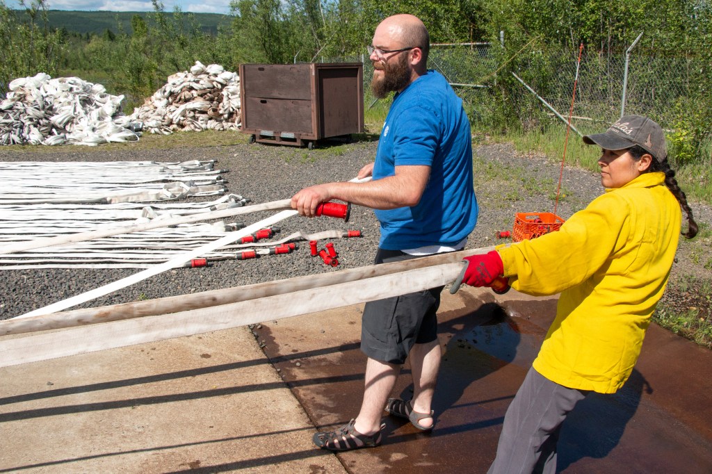Cache materials handlers Morgan Kotche, on left, and Yolanda Copple move hoses over to be tested for leaks at what is called the hose pond at BLM AFS facilities on Fort Wainwright June 3, 2019. The hose must hold water at 300 psi for three minutes.