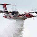 Red double-propeller airplane with black and red stripes drops water while airborne.