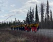 A line of firefighters walking down a gravel road cutting through a firest.