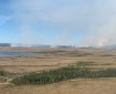 Photo of a flat tundra landscape with wispy smoke columns.
