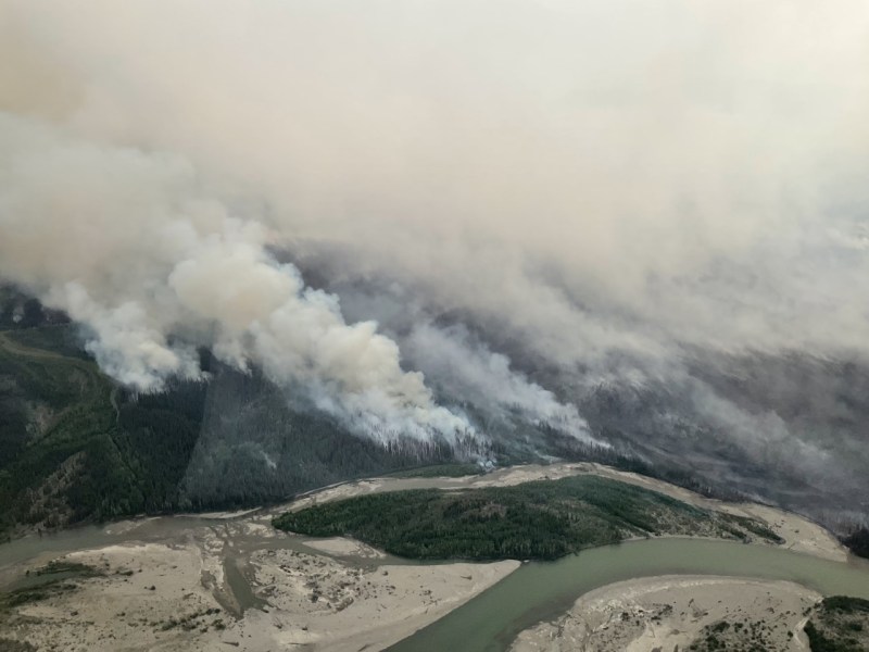 Photo of forested landscape with wildfire smoke rising into the air.