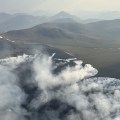 smoke pours from a large tundra fire with mountains in the distance