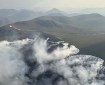 smoke pours from a large tundra fire with mountains in the distance