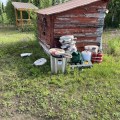 A picture of fire hoses stacked in front of a red shed. Showing grass and trees in the background.