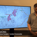 Man stands next to a tv displaying a map of the Dalton Highway Complex. Banner along bottom of image reads Billy McCall Dalton Highway Complex Incident Commander