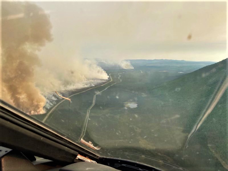 Landscape seen from the cockpit of an airplane, showing smoke from fire burning next to a road. Alaska pipeline follows the same route as the road but is on the other side of the road from the fire. Purpose: showing location of wildfire edge on landscape.