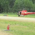A helicopter assigned to the Bean Complex of wildfires sits on the ground with rotors stopped and firefighters nearby at the Manley Hot Springs Alaska airstrip.