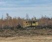 A yellow bulldozer pushes a berm of dirt, brush, and trees with burned area in background and bare dirt in foreground.
