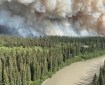 A plume of smoke raises above black spruce forest along a small river.