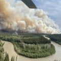 A plume of smoke rises over a black spruce forest and river bend.