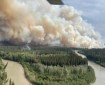 A plume of smoke rises over a black spruce forest and river bend.