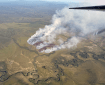 Smoke drifts up from a fire burning through green tundra.