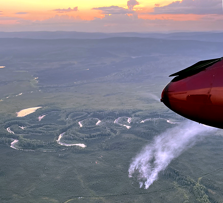 Aerial view of smoke driving up from a fire with a pink sky in the background.
