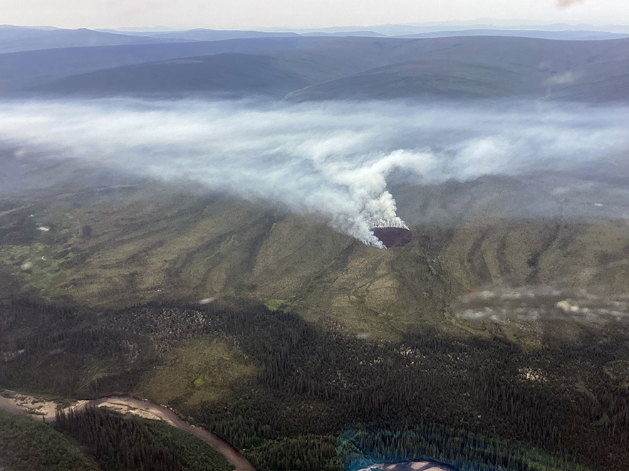 Smoke drifts up from a fire that burned a round patch of land atop a mountain.