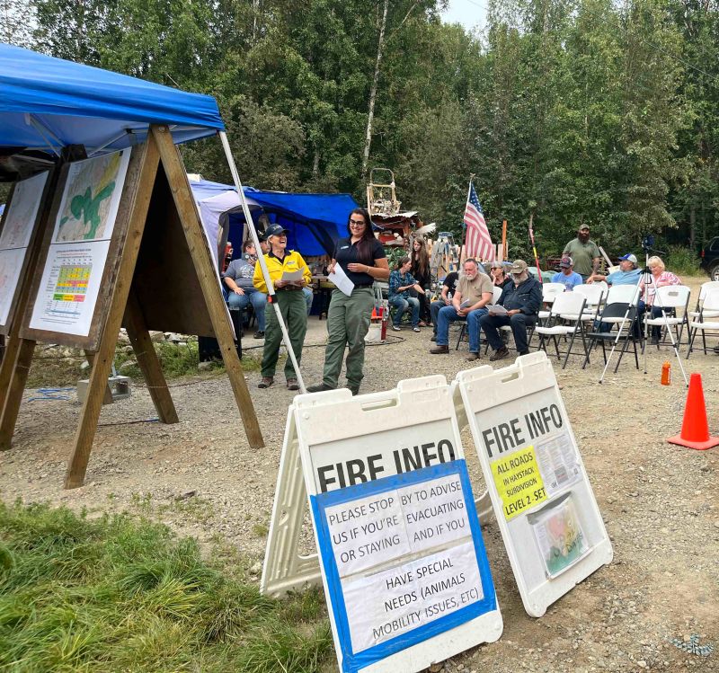 People gather around information boards and in chairs for a community meeting.