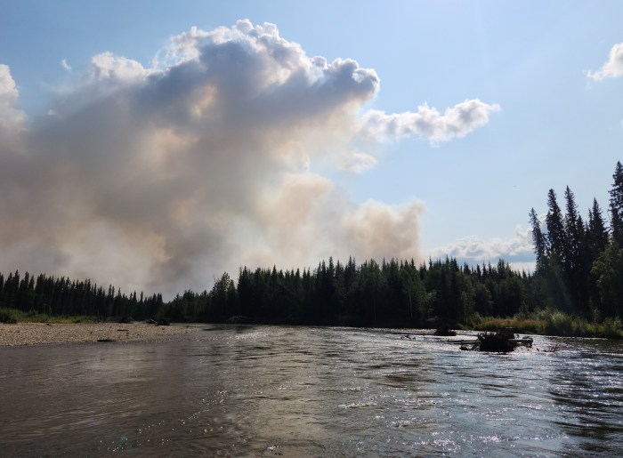 A large column of smoke rises above a river,