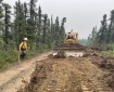 A firefighter and heavy equipment work to build fire break.