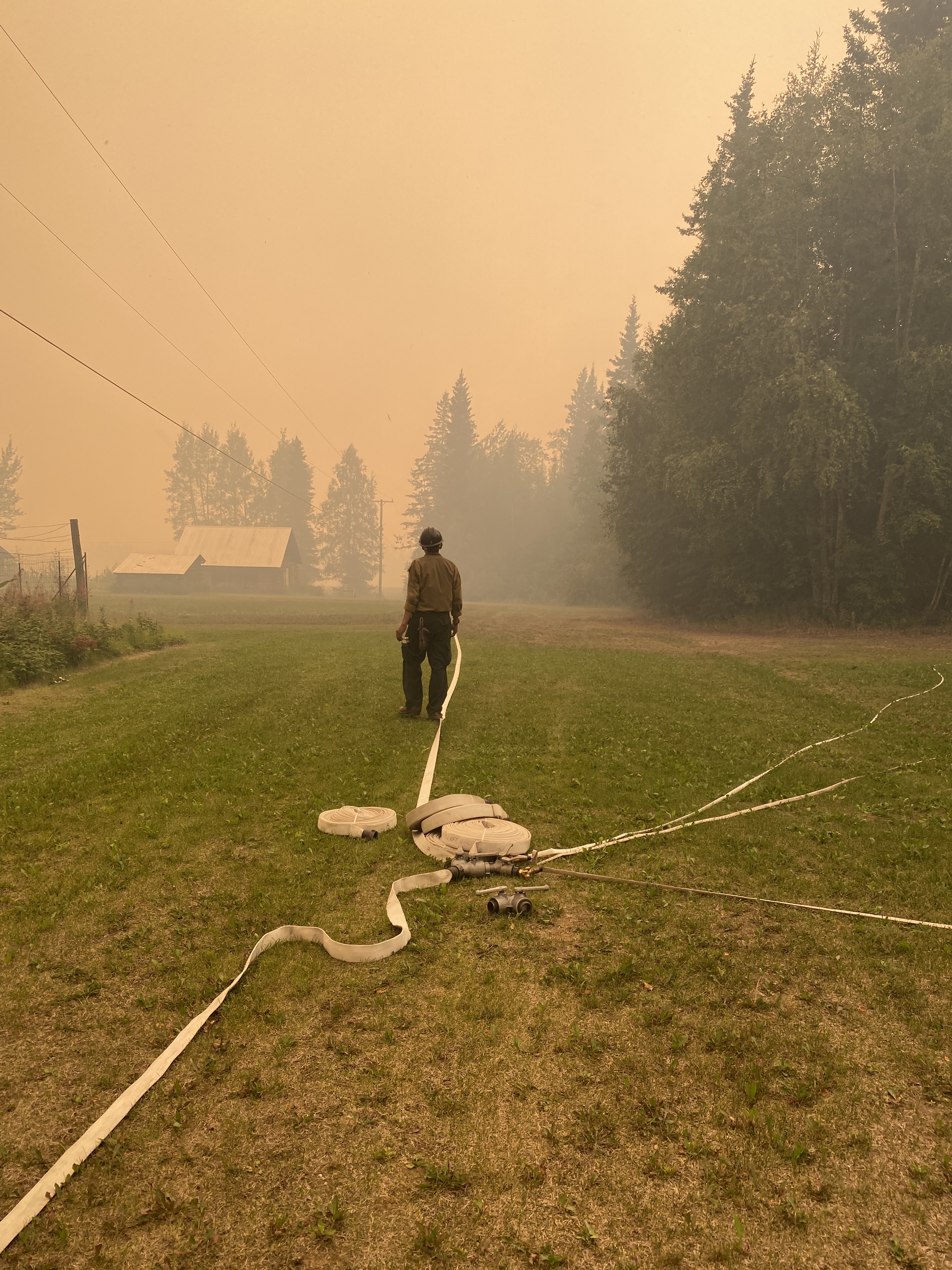 A firefighter stands by fire hoses on the ground in a smoky field