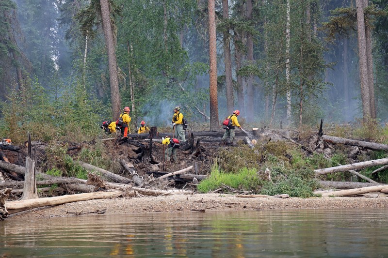Firefighters on the bank of the Salcha River mopping up a burned area. They are spraying water and scraping burned logs.