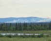 Tundra, lake and spruce foreground with two smoke plumes rising in front of mountains.