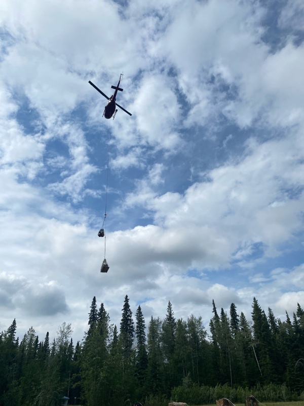A medium helicopter lifting a daisy chain with equipment. Skies are partly cloudy.