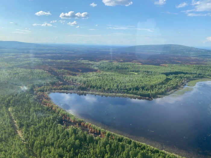 Mostly sunny day aerial view of the fire showing burned and unburned area around a lake.