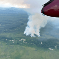 smoke rises up from a forest fire as seen through the open door of an airplane.