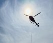 A helicopter hovers with a cable extending to the ground.