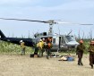 Helicopter in center of the frame with several firefighters in yellow shirts help remove supplies from the helicopter and firefighters in orange hard hats exit and walk toward the camera and to the right of the frame.