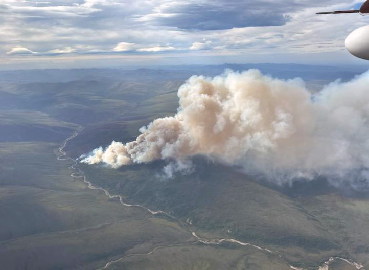 A large smoke column rises up from a burned area right of a creek.