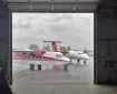 Two red and white airplanes as seen looking through the doorway of a cargo pay.