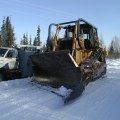 Photo of a dozer with a shear blade attachement. The dozer is next to a large work truck in a wooded area on a snowy road.