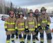 A group of 6 structure firefighters stand in a line in uniform. They are outside in a snowy setting.