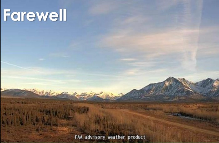 An airstrip surrounded by a large field-like area covered in dry brown grass and brush. There are snow-capped mountains in the background.