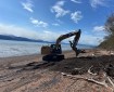 An excavator extinguishes a fire on a beach.