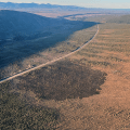 A dark burned patch of land next to a roadway with mountains in the background.