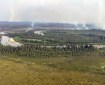 Forest and tundra in the foreground with a river going from left to right through the photo. Wildfire smoke rises from the forested areas in the background.