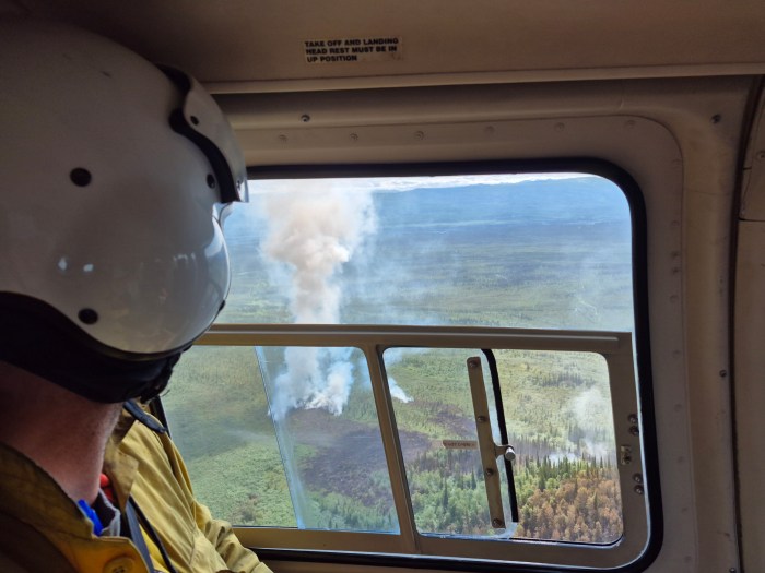 A smoke plume rises, seen from a helicopter window.