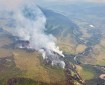 Aerial photo showing wildfire smoke rising from a forested area with a creek on the right side of the image.
