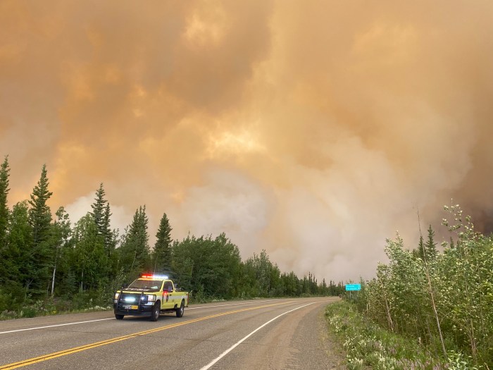 Fire engine on road with smoke and trees and in the background.