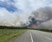 Smoke billows up from a forest fire burning on both sides of a highway.