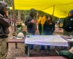 Several people in nomex pants and sweatshirt gather around a table under a yellow tarp, looking at a map.