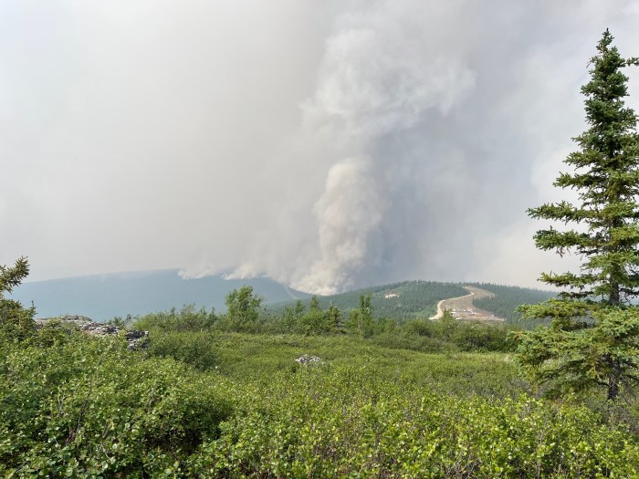 a large smoke plume in the background of multiple green hills of foresr
